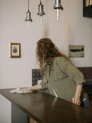 A woman with curly hair wipes a kitchen counter in a beautifully decorated home interior.